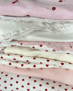 Stack of folded white and pink clothes with lace trim and heart patterns