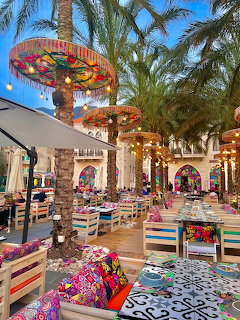 Colorful outdoor restaurant courtyard with decorated tables, umbrellas, arches, and palm trees