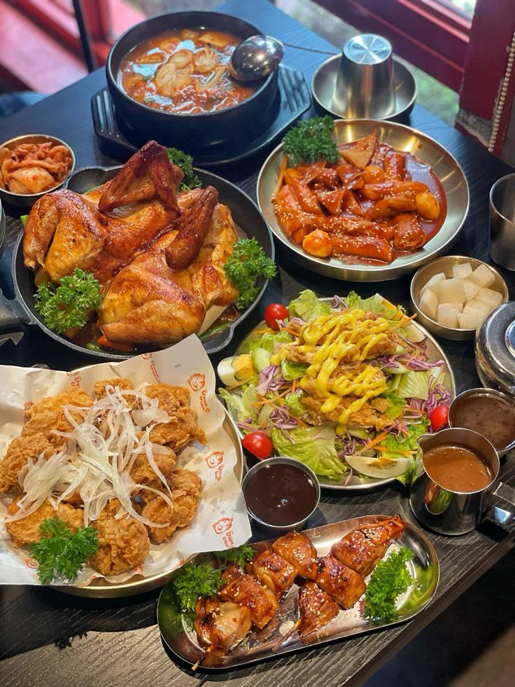 Table covered with plates of Korean fried chicken, spicy wings, kimchi, salad, bean sprouts, and sauces