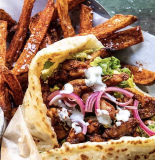 Pita wrap filled with meat, onions, lettuce, sauce, and fries beside it