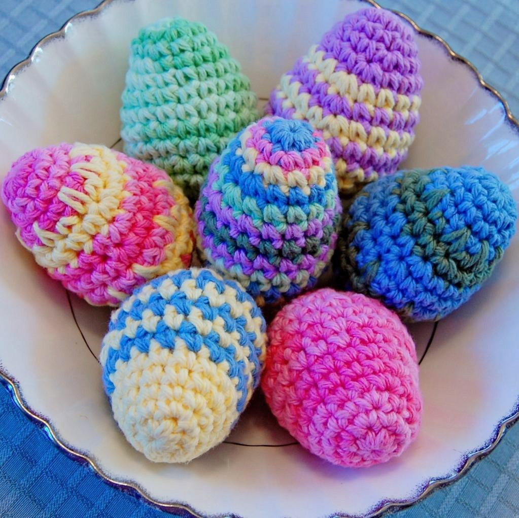 Seven colorful crocheted Easter eggs with striped patterns displayed on a white plate