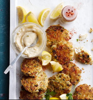 Several golden crab cakes with lemon wedges and white dipping sauce