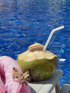 Green coconut with white straw on a white chair beside a blue swimming pool