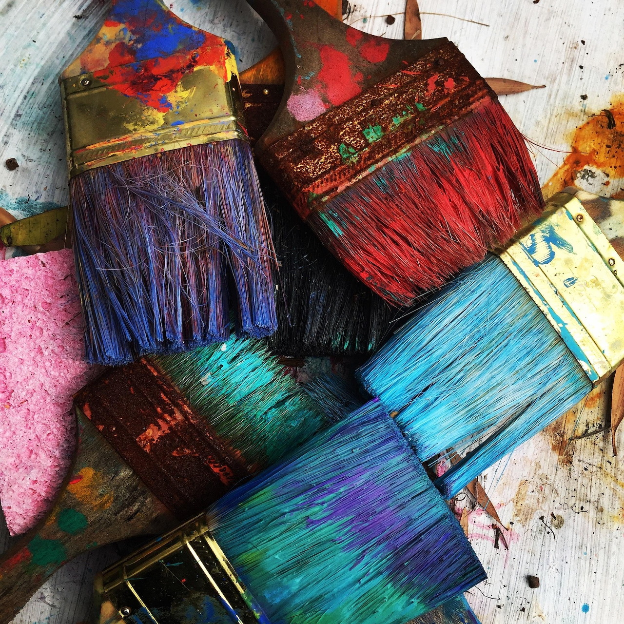 Close-up of colorful paint-covered artist brushes with blue, red, and purple bristles on a paint-splattered surface