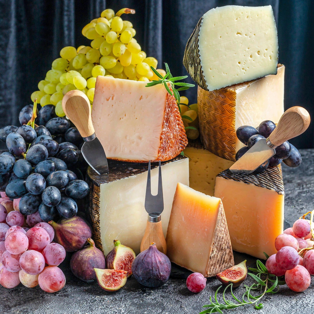 Assorted cheese wheels and wedges with grapes and figs on slate board