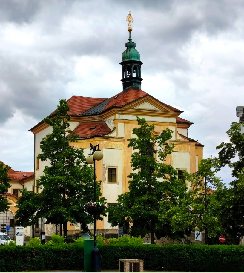 Baroque church with green dome and golden spire surrounded by trees in Benešov, Czech Republic