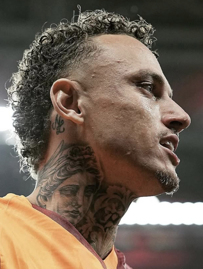 Close-up of a man with curly hair and elaborate neck tattoos wearing an orange sports jersey