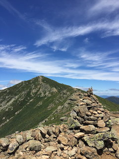 Rocky mountain ridge trail with blue sky and wispy clouds overhead