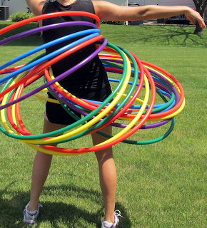 Girl with multiple rainbow colored hula hoops spinning around waist on grass lawn