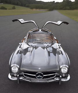 Silver Mercedes 300 SL with gullwing doors raised open on a road