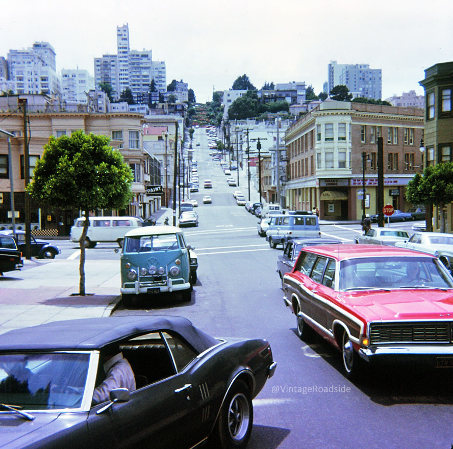 Vintage cars driving on a steep San Francisco street lined with buildings and trees