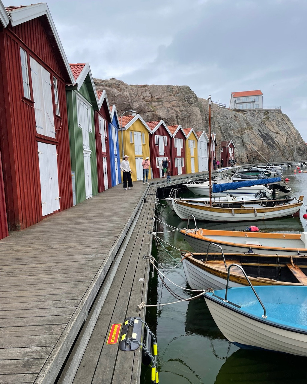 Red and white wooden huts along Smögen harbor with boats and rocky shore