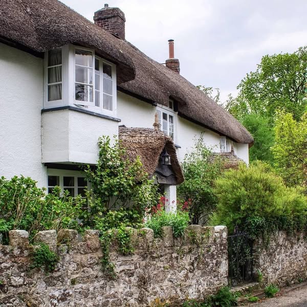 White thatched cottage with garden behind stone wall