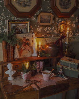 Candlelit vintage sideboard with Little Women book, pine branches, teacup, bust figurine, and framed prints.