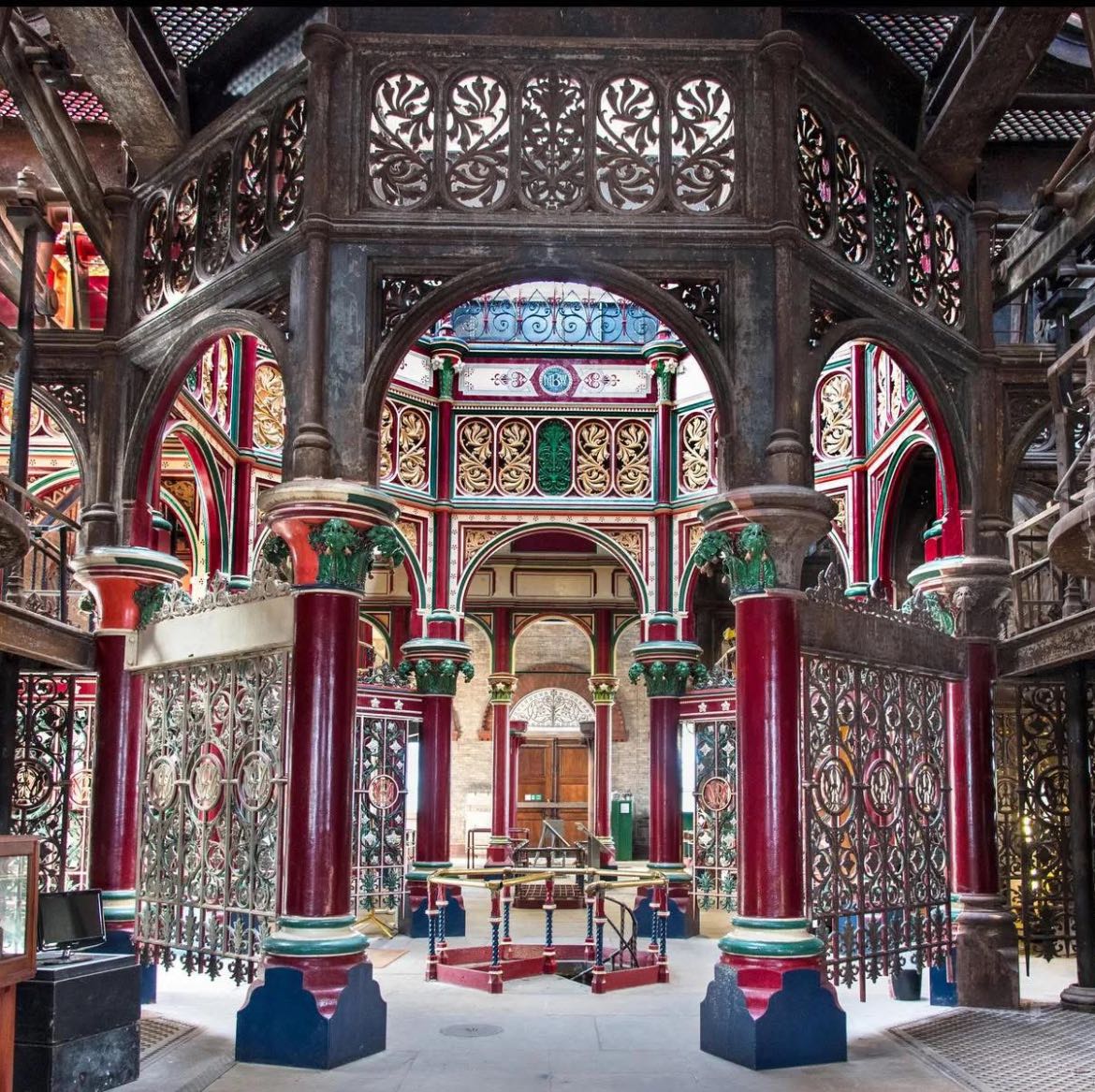 Ornate Victorian pumping station interior with colorful ironwork, stained glass, and red columns