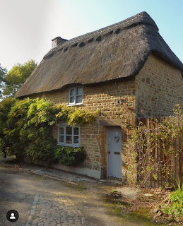 Small brick cottage with a thatched roof beside a cobblestone path