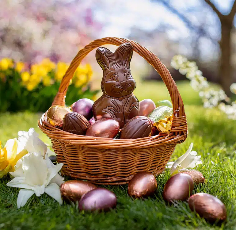 Wicker basket with a chocolate bunny and chocolate eggs on grass with spring flowers