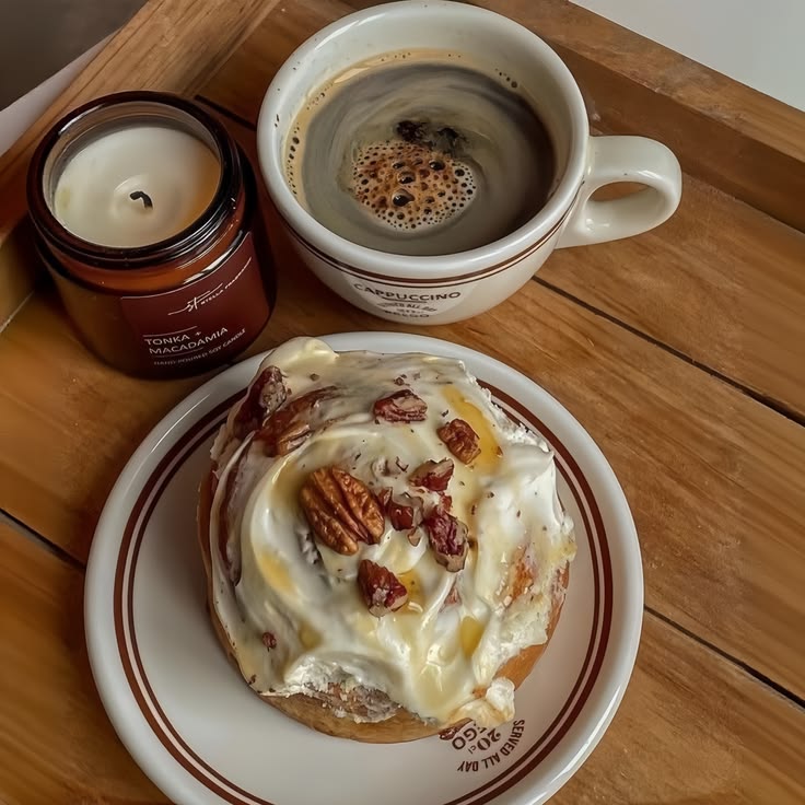 Cup of coffee, iced cinnamon roll with pecans, and a candle on a wooden tray