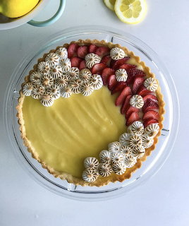Overhead view of a lemon tart with piped meringue and fresh strawberry slices on a glass plate