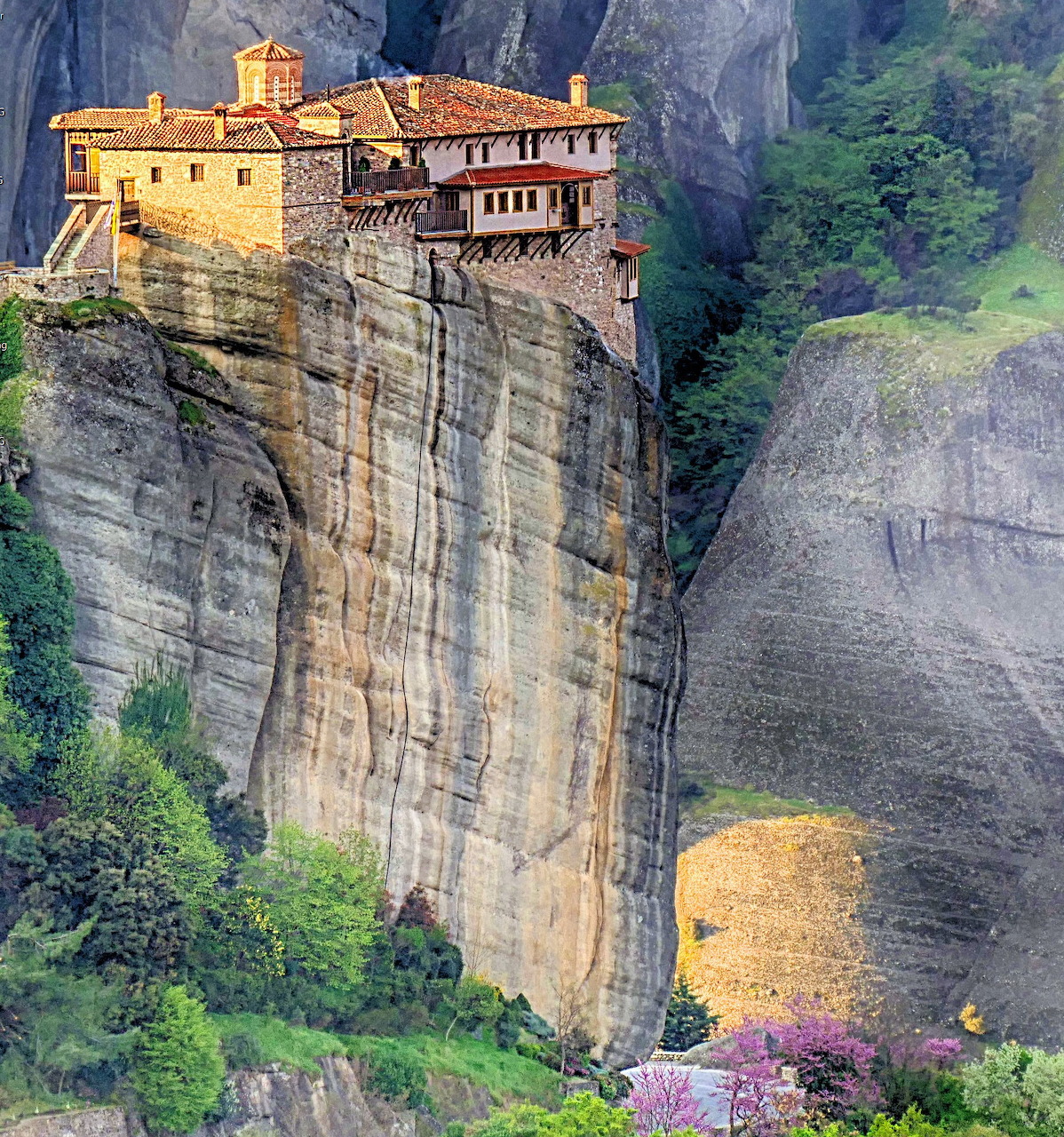Monastery built atop a sheer sandstone cliff at Meteora, Greece, with green trees below