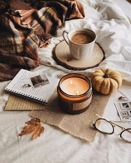 Cozy fall flatlay with candle, coffee, pumpkin, autumn leaves, notebook, and plaid blanket