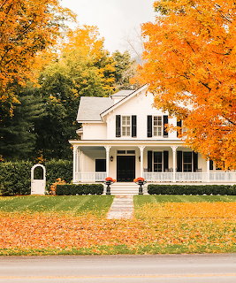 White colonial house with front porch surrounded by orange and yellow autumn trees