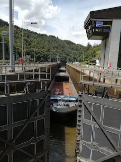 Barge navigating through a river lock with concrete walls and a control tower surrounded by green hills