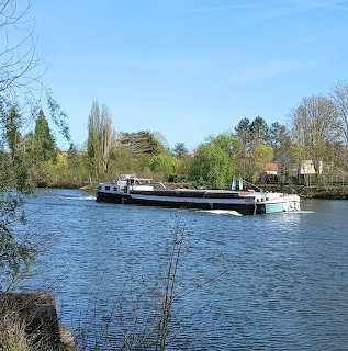 Long barge on a river with trees and houses under a blue sky