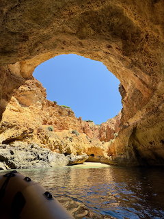 View through a cave opening showing blue sky, rocky cliffs, and calm ocean water in Portugal