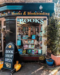 Quaint bookshop entrance with turquoise awning, books displayed in window and on sidewalk racks