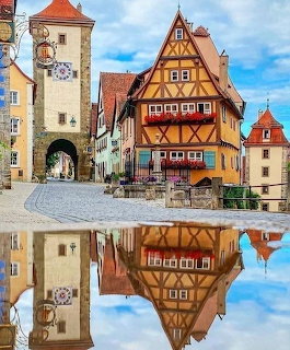 Colorful half-timbered houses and stone tower in Rothenburg ob der Tauber reflected in a puddle