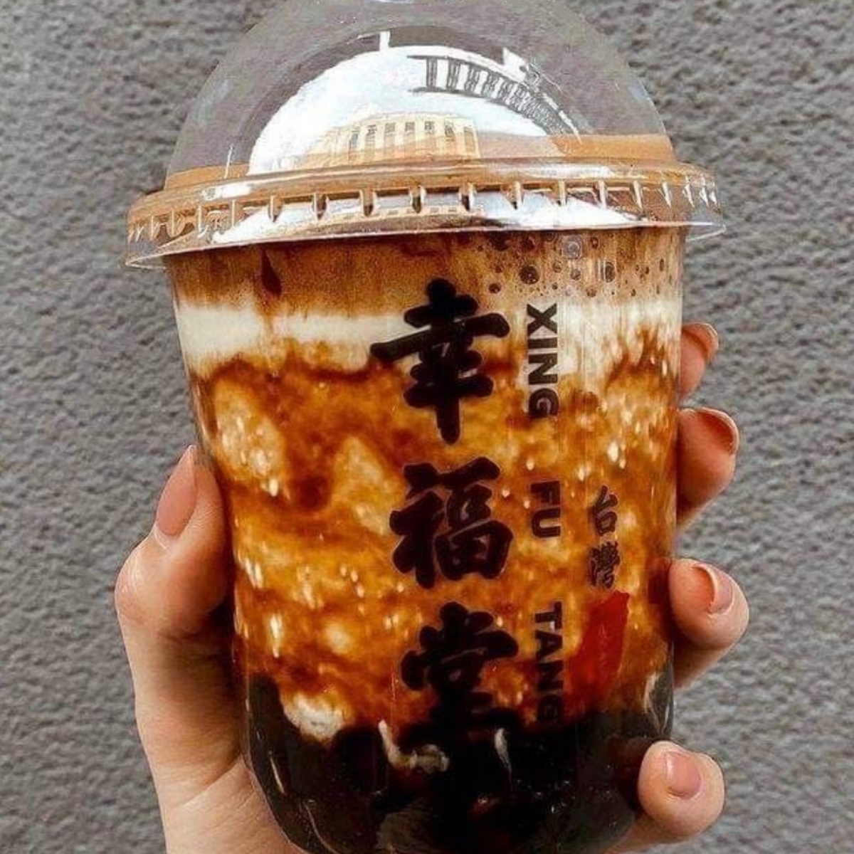 Hand holding layered boba milk tea with tapioca pearls in clear cup