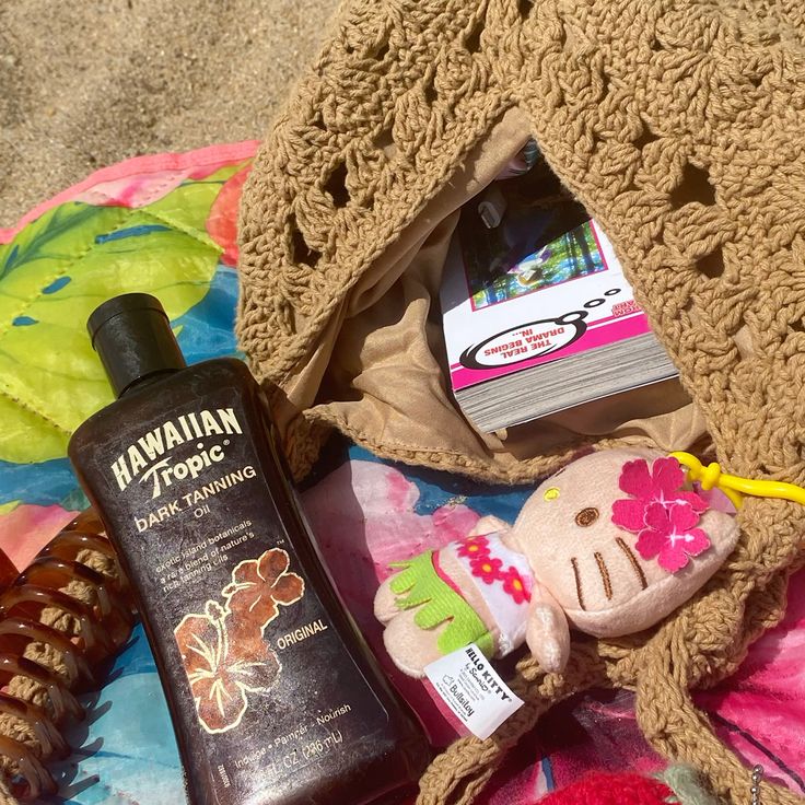 Beach towel on sand with woven bag, tanning oil bottle, and small accessories