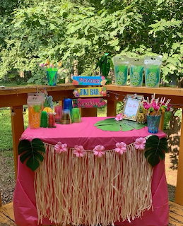 Vibrant tropical tiki bar with pink table, colorful cups, decorations, and lush green background