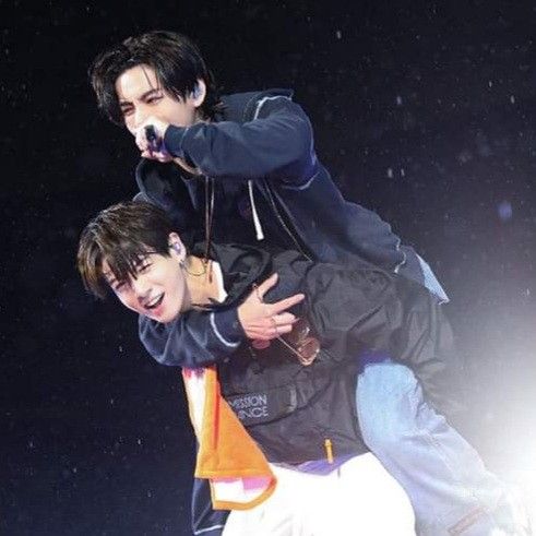 Two K-pop idols embracing on stage with spotlights and starry background