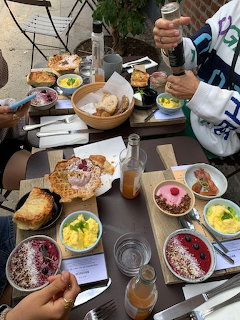 Overhead view of an outdoor brunch table with smoothie bowls, waffles, scrambled eggs, and juice bottles