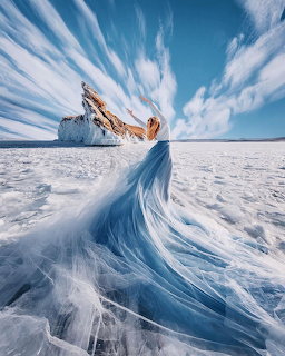 Woman in long blue dress standing on frozen Lake Baikal with dramatic clouds and ice formation