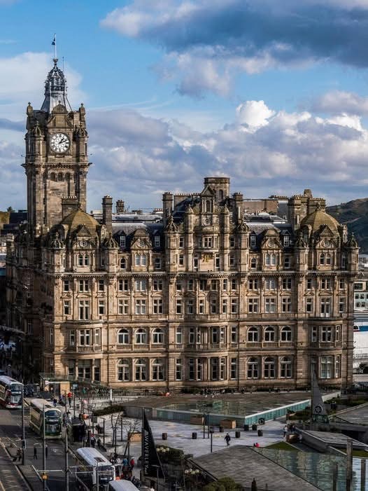 Balmoral Hotel and clock tower in Edinburgh with city streets and buses below under cloudy sky