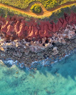 Aerial view of red cliffs meeting turquoise ocean with green vegetation in Broome, Australia