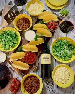 Colorful Mexican ingredients in yellow bowls on rustic wooden table with wine bottle
