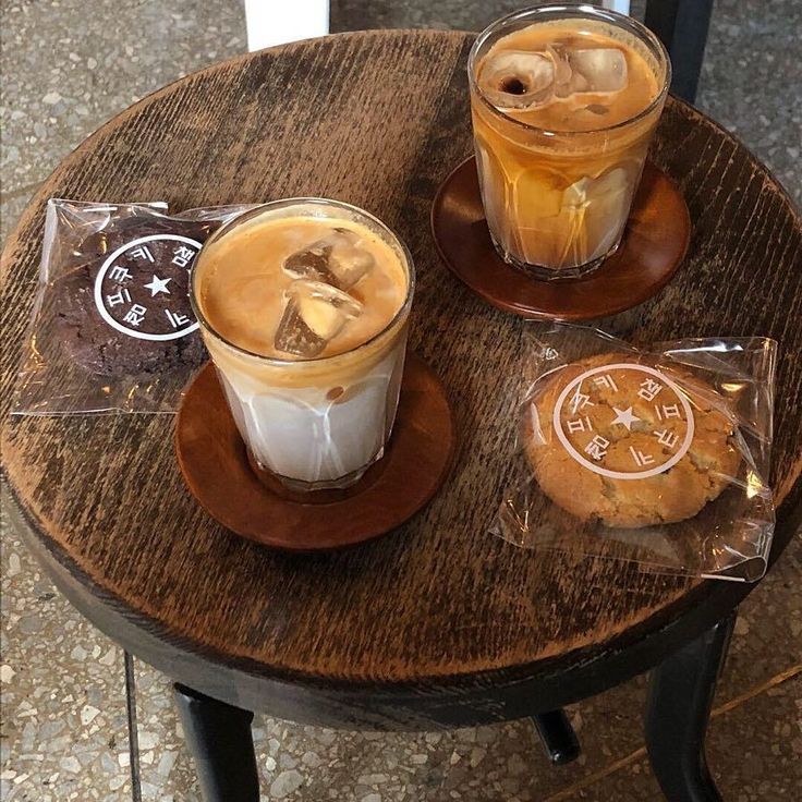 Two iced lattes and packaged cookies on a round rustic wooden cafe table