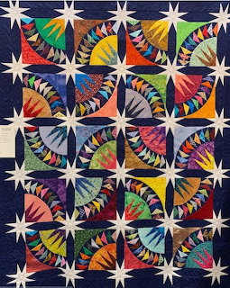 Patchwork quilt with white stars and colorful geometric fan patterns in repeating square blocks