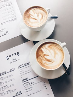Two white cups of latte with latte art sitting on cafe menus on a table