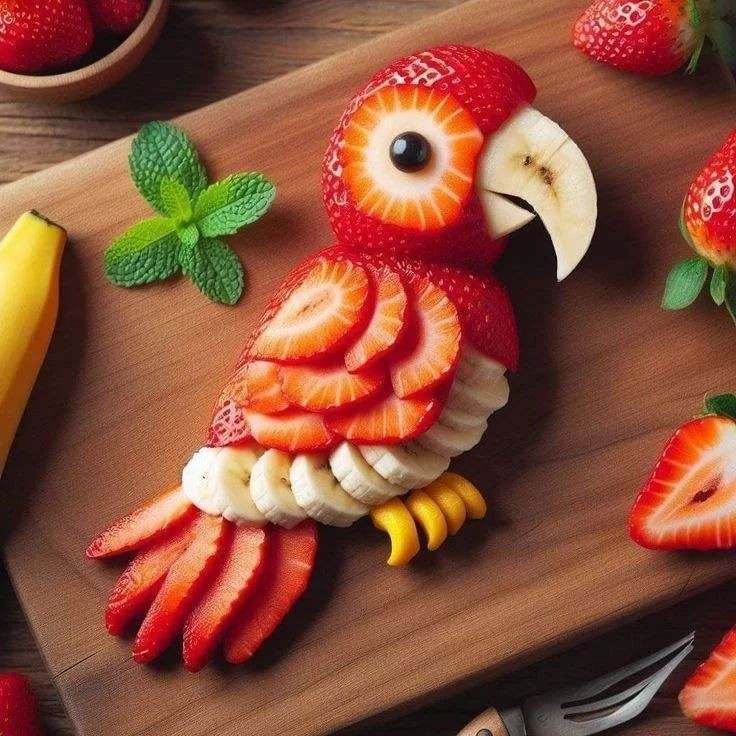 Fruit arranged into a bird shape on a wooden cutting board with strawberries, banana, and mint