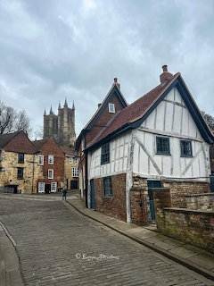 Cobbled street in Lincoln with old timber-framed houses and cathedral towers in the distance.