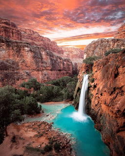Waterfall flowing into bright turquoise pool in red rock canyon at sunset