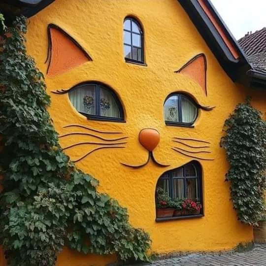 Yellow house facade painted to resemble a cat face with window eyes, orange nose, and whiskers