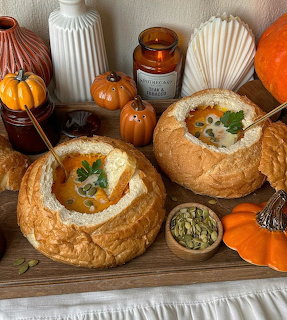 Two bread bowls filled with creamy soup, garnished with herbs, surrounded by decorative pumpkins and autumn decor