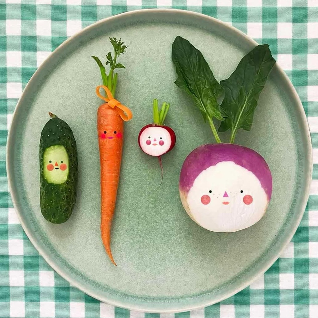 Illustrated vegetables with kawaii faces arranged on a ceramic plate over green gingham tablecloth