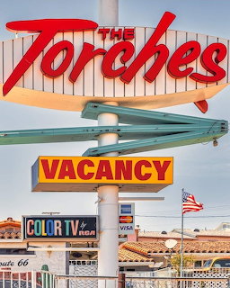 Vintage roadside motel sign with red 'The Torches' neon text and turquoise arrow against blue sky